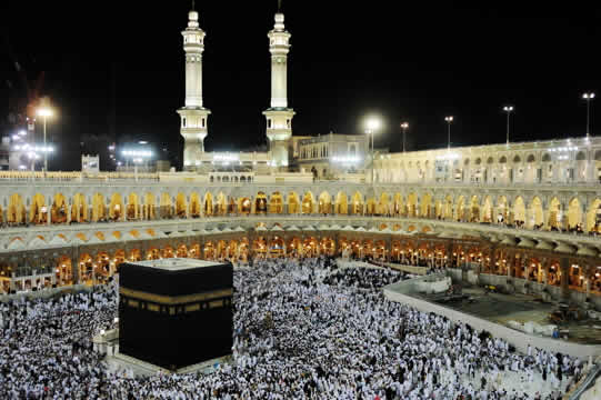 large black building surrounded by thousands of people in white, at night