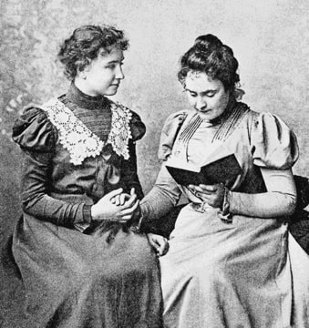 Photograph of the two women holding hands, Sullivan is reading from a book