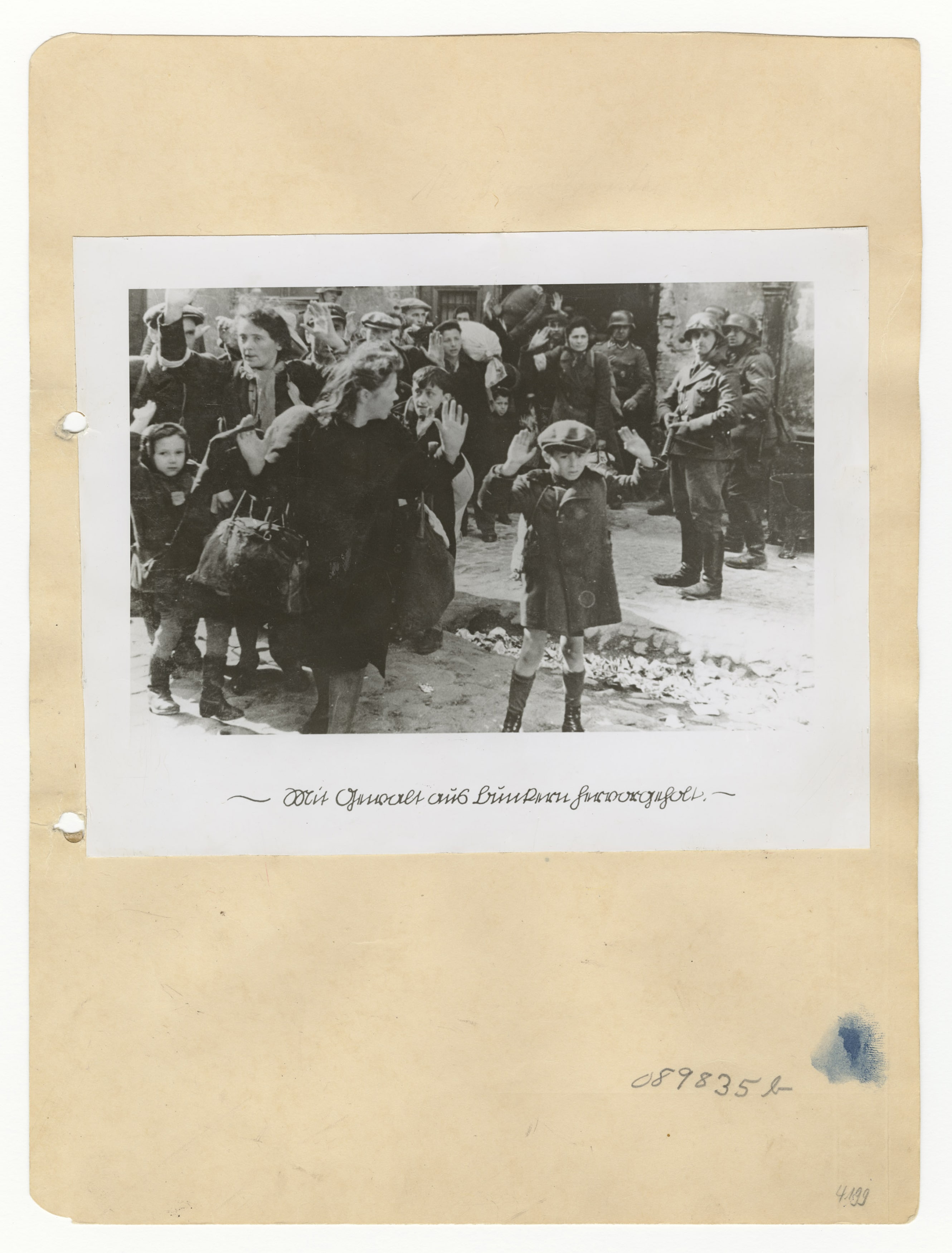 historic photo of a group of people exiting a building carrying bundles and surrounded by soldiers; in the front a young boy stands with his hands up in surrender