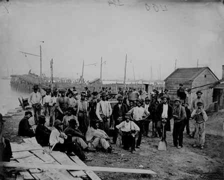 Photograph of many laborers sitting and standing around the waterside