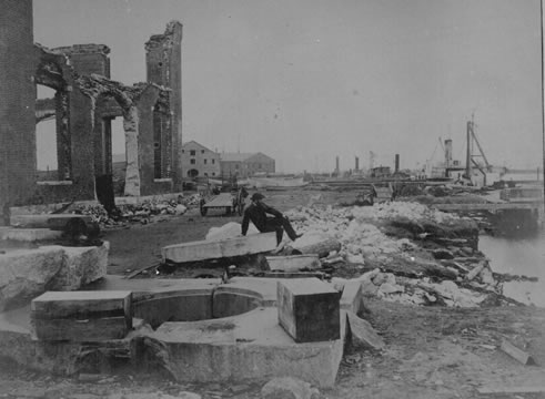 Photograph of man sitting by the waterside amidst rubble and ruins