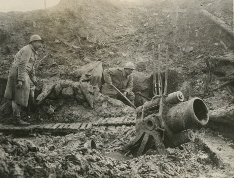 photograph of a soldier digging in a trench while another soldier walks toward a mortar