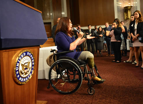 Democratic Senator Tammy Duckworth of Illinois sitting in a wheelchair, addressing a group of visitors in the Senate chamber