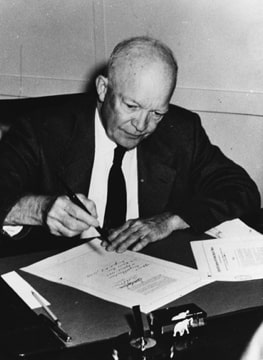 photograph of Eisenhower at his desk signing the text of the bill