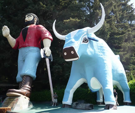 statue of a man in a red shirt and blue pants holding an axe, alongside a big blue bull