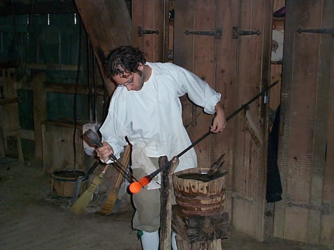 a colonist is working with red-hot glass in a colonial-style workshop