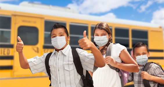 students wearing face masks in front of a school bus
