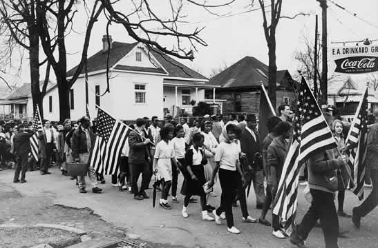 photograph of mainly Black men, women, and children marching peacefully with American flags back