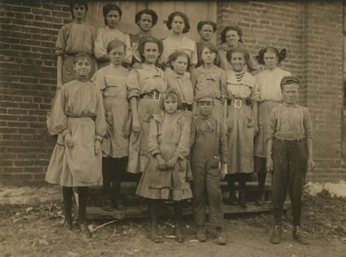 an old photograph of a group of children and young adults standing in front of a brick building