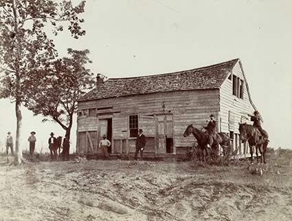 men, some on horseback, around a large wooden building