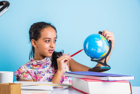 Photograph of girl pointing to a small globe with a pencil