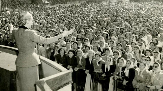 a woman standing on a balcony addressing a large crowd of women