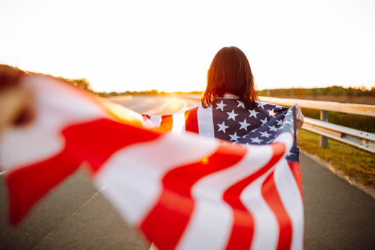 back view of a girl walking down a road with a flag waving behind her