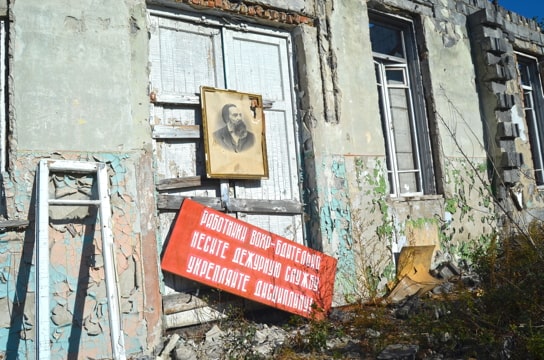 an old building, all boarded up, with a large red sign and a photo of Karl Marx on the door