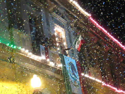 A lit window in a large stone building with flags and banners flying and confetti coming down