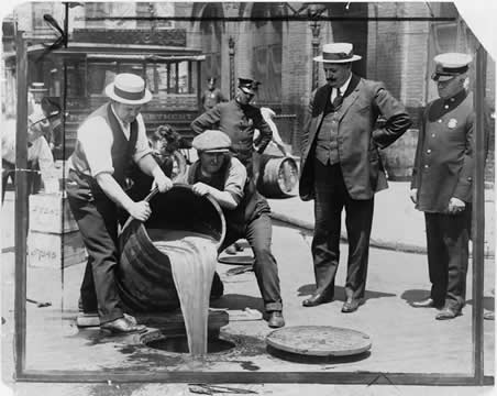 two men pouring a barrel of liquid down a drain hole while others look on