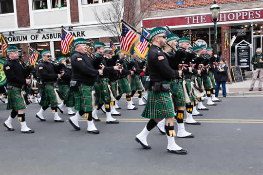 rows of bagpipe players dressed in green kilts and berets, carrying American flags