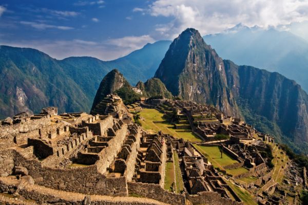 Stone ruins and terraces of Machu Picchu in the Andes Mountains of Peru, with steep green mountains rising in the background.