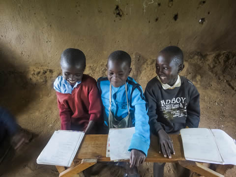 three boys sit at desks, smiling